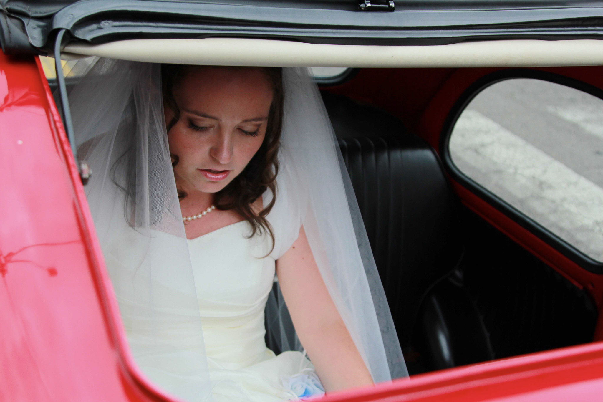 Una sposa incorniciata dal finestrino di un’auto d’epoca rossa